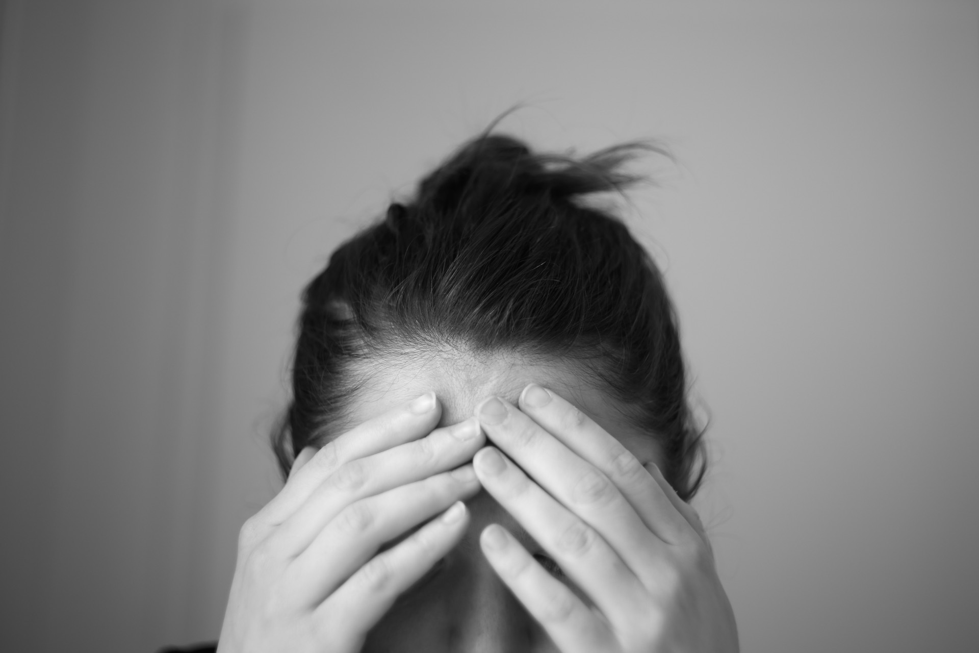 A person sitting in low light with a hand pressed to their forehead